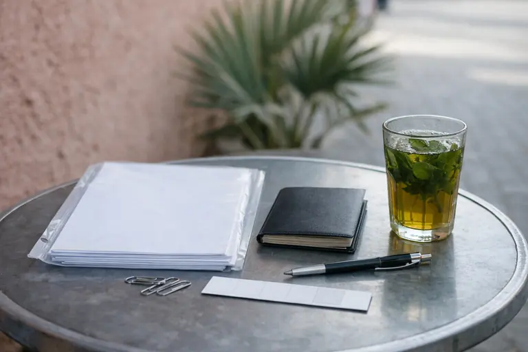 Illustration : pochette de documents, passeport fermé et verre de thé sur une table de terrasse
