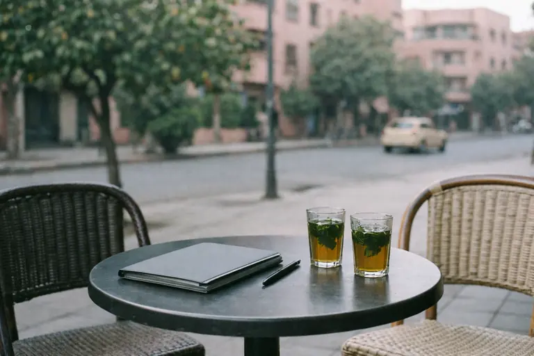 Illustration : table de terrasse avec deux chaises vides, une pochette et deux verres de thé